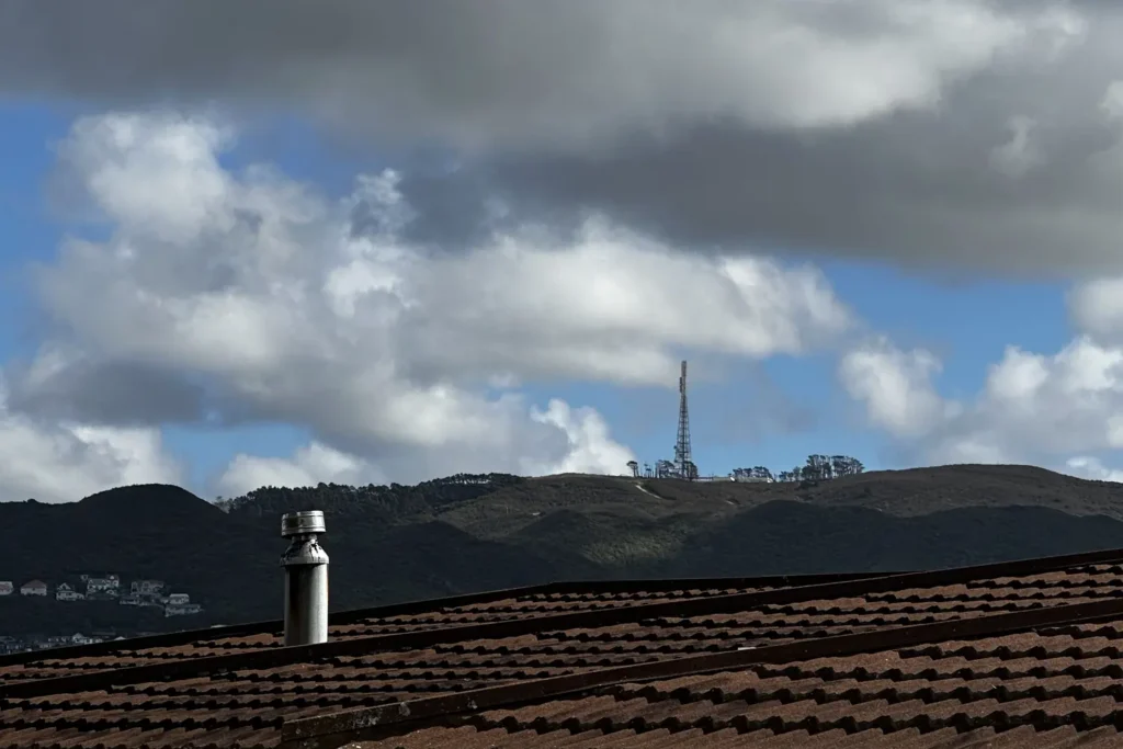 Wood burner flue on a tiled roof with the northern Wellington hills and Mount Kaukau transmission tower behind
